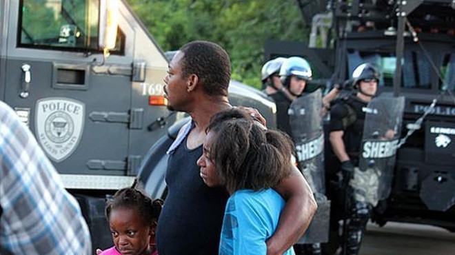 A family watches police in riot gear move into Ferguson in the early days of the August protests.