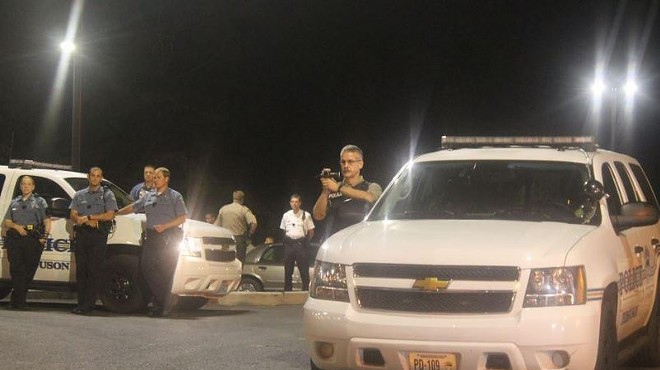 A St. Louis County police officer records protesters in front of the Ferguson Police Department.