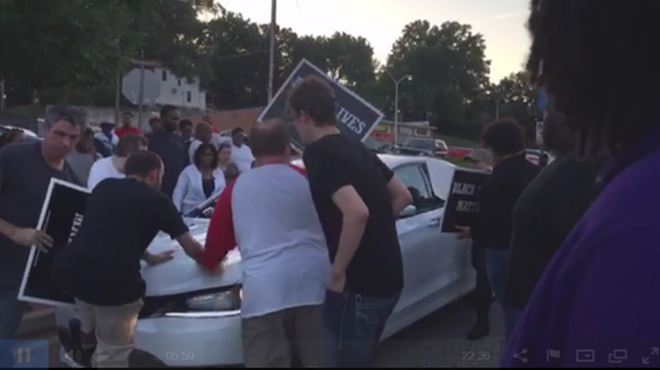 Protester Phillip Weeks (at left with sign) backpedals away from a Chrysler driving through a demonstration in Ferguson.