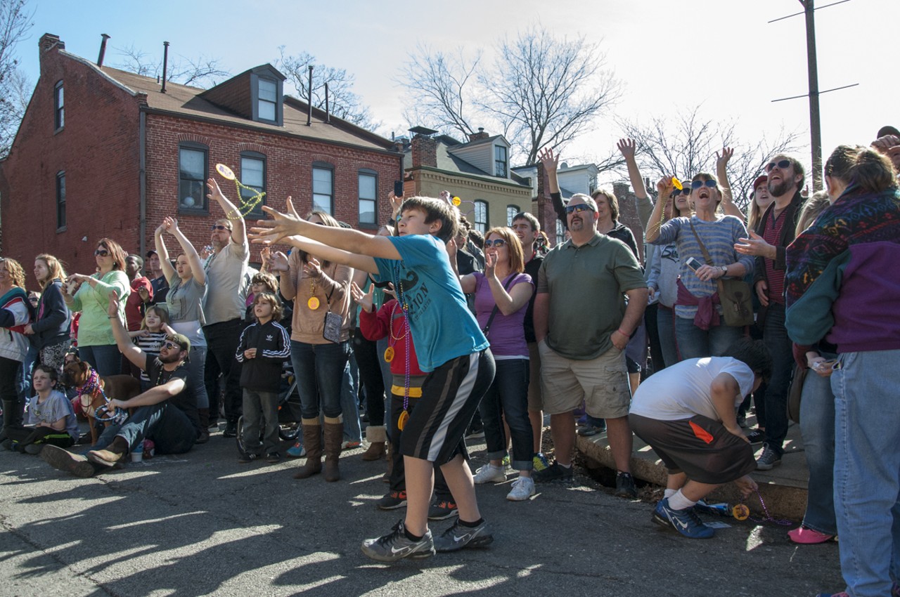 A kid in the crowd leaps out to catch some beads thrown from a parade float.