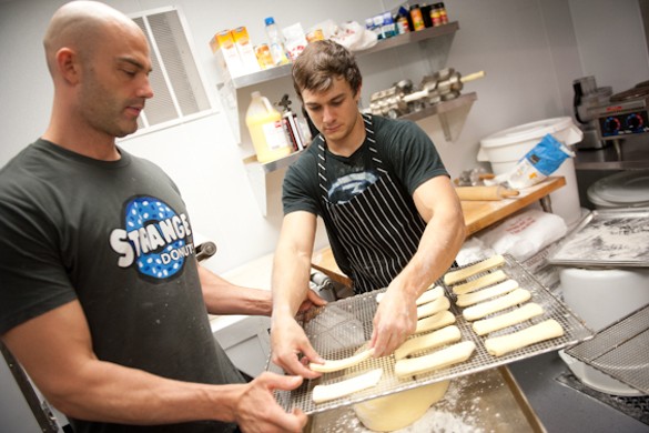 Jason Bockman, left, and Tyler Fenwick, right, work in the kitchen as patrons begin lining up outside Strange Donuts.