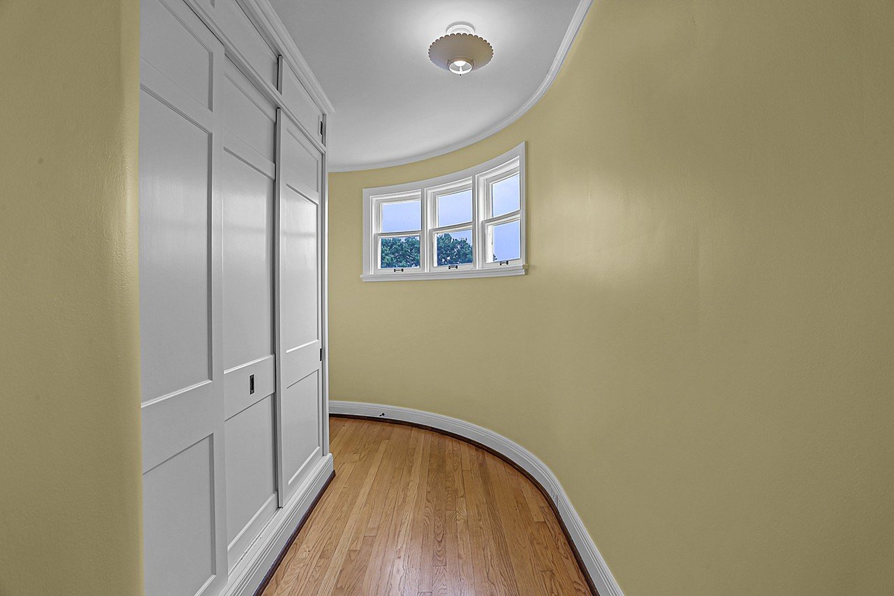 The curved hallway leads to the shared bathroom between the two kids' bedrooms. It features built-in cabinetry, with copper clothes rods.