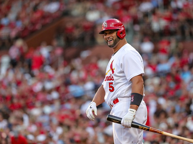 Albert Pujols smiles in a Cardinals uniform with a bat in his hand.