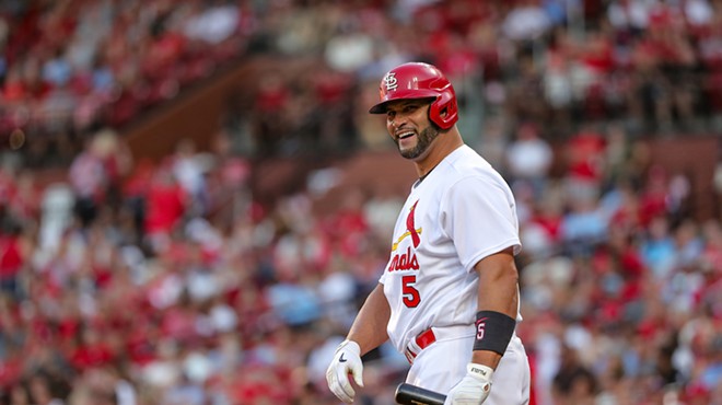 Albert Pujols smiles in a Cardinals uniform with a bat in his hand.