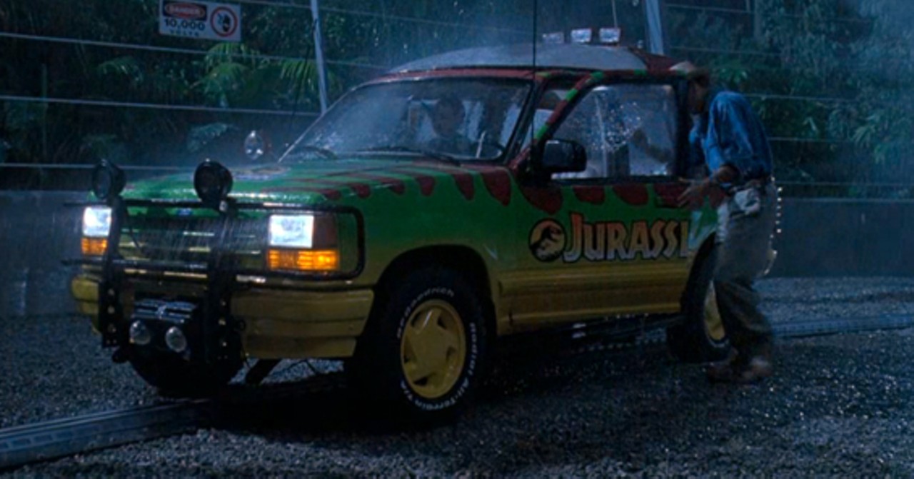 Dr. Grant returns to his vehicle after checking on the kids in their identical Jurassic Park-branded SUV. This shot clearly establishes the scene's geography and the characters' place in it.