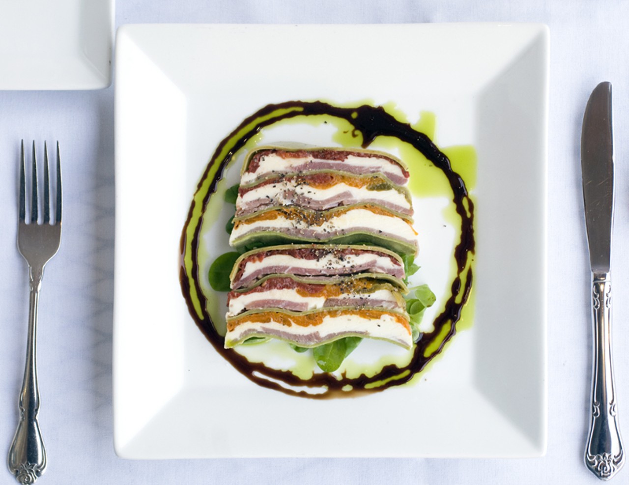 The Heirloom Tomato Terrine is a sliced loaf of heirloom tomatoes, paper-thin prosciutto, fresh mozzarella, house-made spinach pasta, baby mache, basil oil and balsamic gastrique.