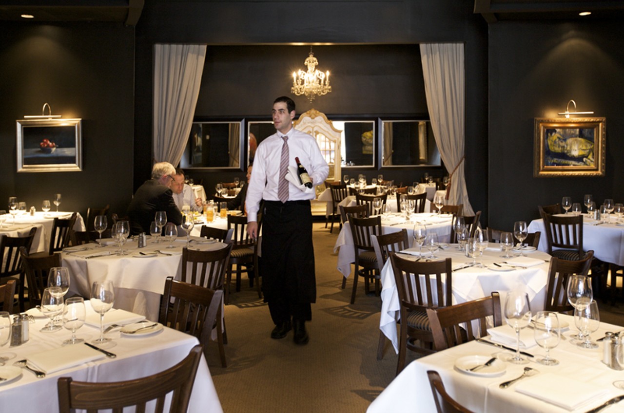 Server David Stiffelman bringing a bottle of wine to a table in the main dining room of Chez Leon.