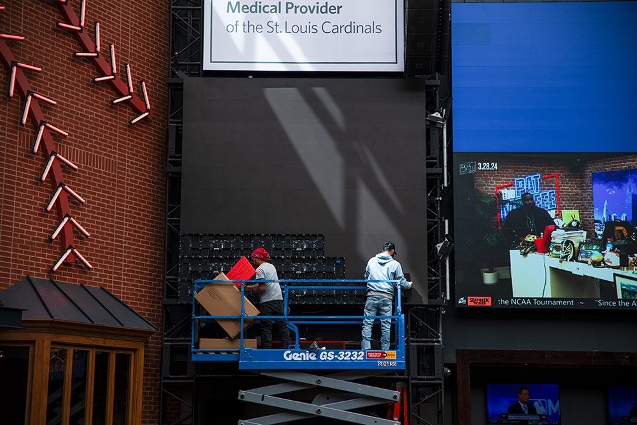 Two workers install a video screen inside Ballpark Village.