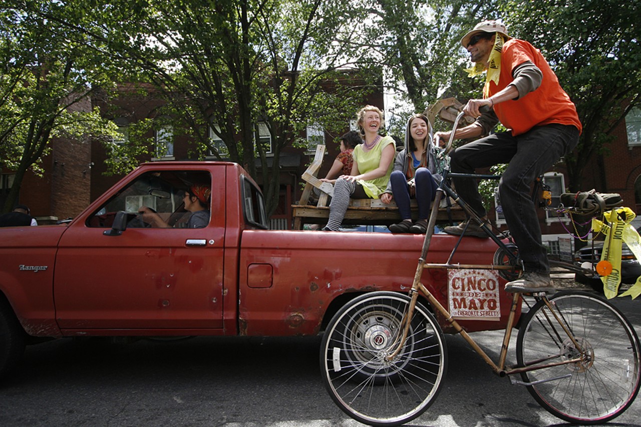 A man on an extra tall bicycle hitches a ride on a truck during the People's Joy Parade.