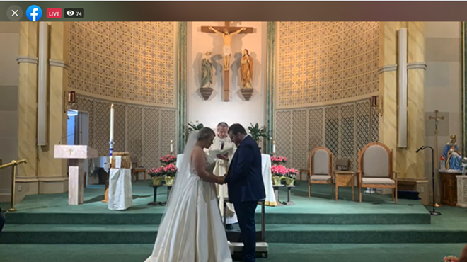Katie and Zach Hawkins bow their heads in prayer as their priest marries them. The two hosted a Facebook live stream to celebrate their wedding during COVID-19.
