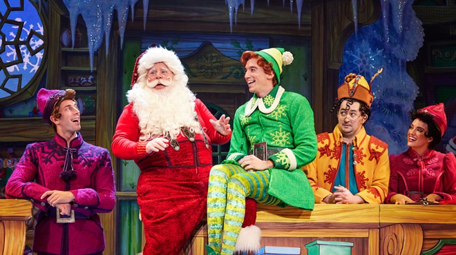 Buddy the elf sits on stage with Santa.