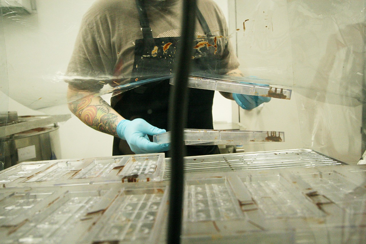 McClure lifts up the plastic covering of a house-made heating cabinet and sifts through chocolate bar molds. By heating the molds to the temperature of the chocolate the resulting chocolate bars will be as shiny as possible.