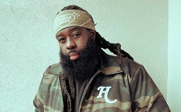 Jas Bell looks at the camera wearing a bandana and a camo jacket with the letter "H."