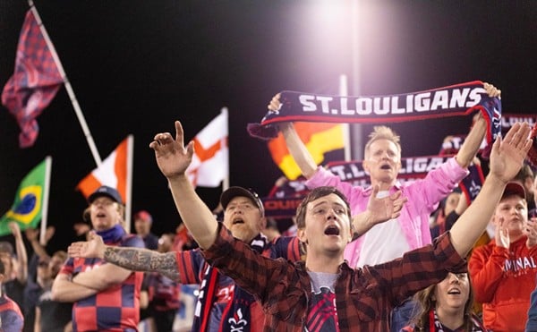 St. Louis soccer fans raise their hands, wave flags, hold up scarves and cheer in the stands.