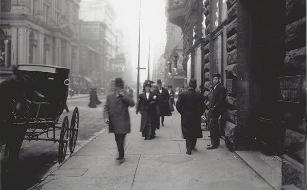 Pedestrians walk on a sidewalk near the intersection of 6th and Locust Streets in St. Louis circa 1900.