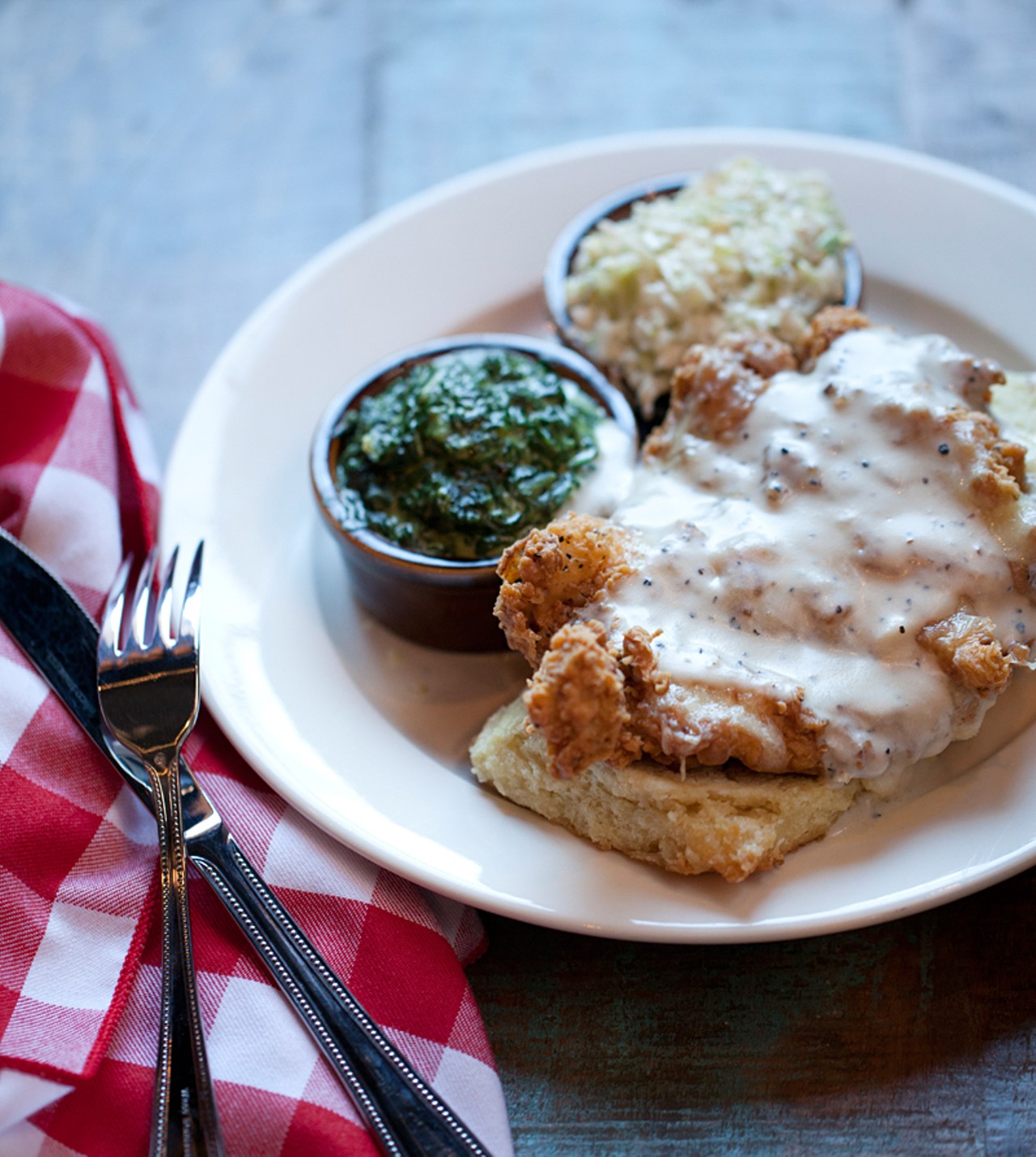 "Chicken in a Biscuit" is buttermilk-fried chicken breast with milk gravy, topped with cheddar cheese and served on a buttermilk biscuit. It's shown here with sides of creamed spinach and slaw.