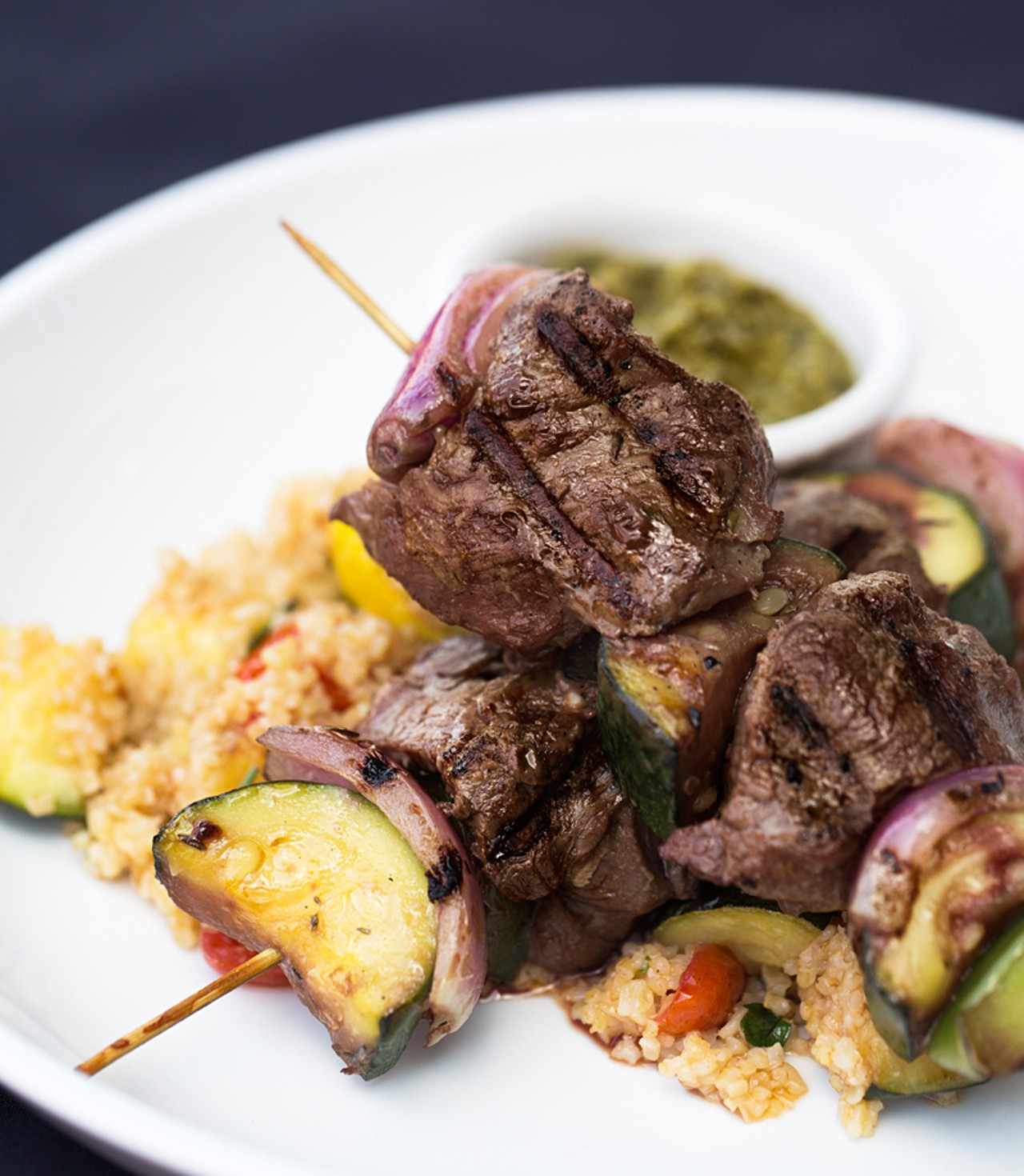 Beef tenderloin kabobs are grilled eight-ounce skewers with squash, zucchini, onions, peppers, warm tabouleh salad and chimichurri sauce.