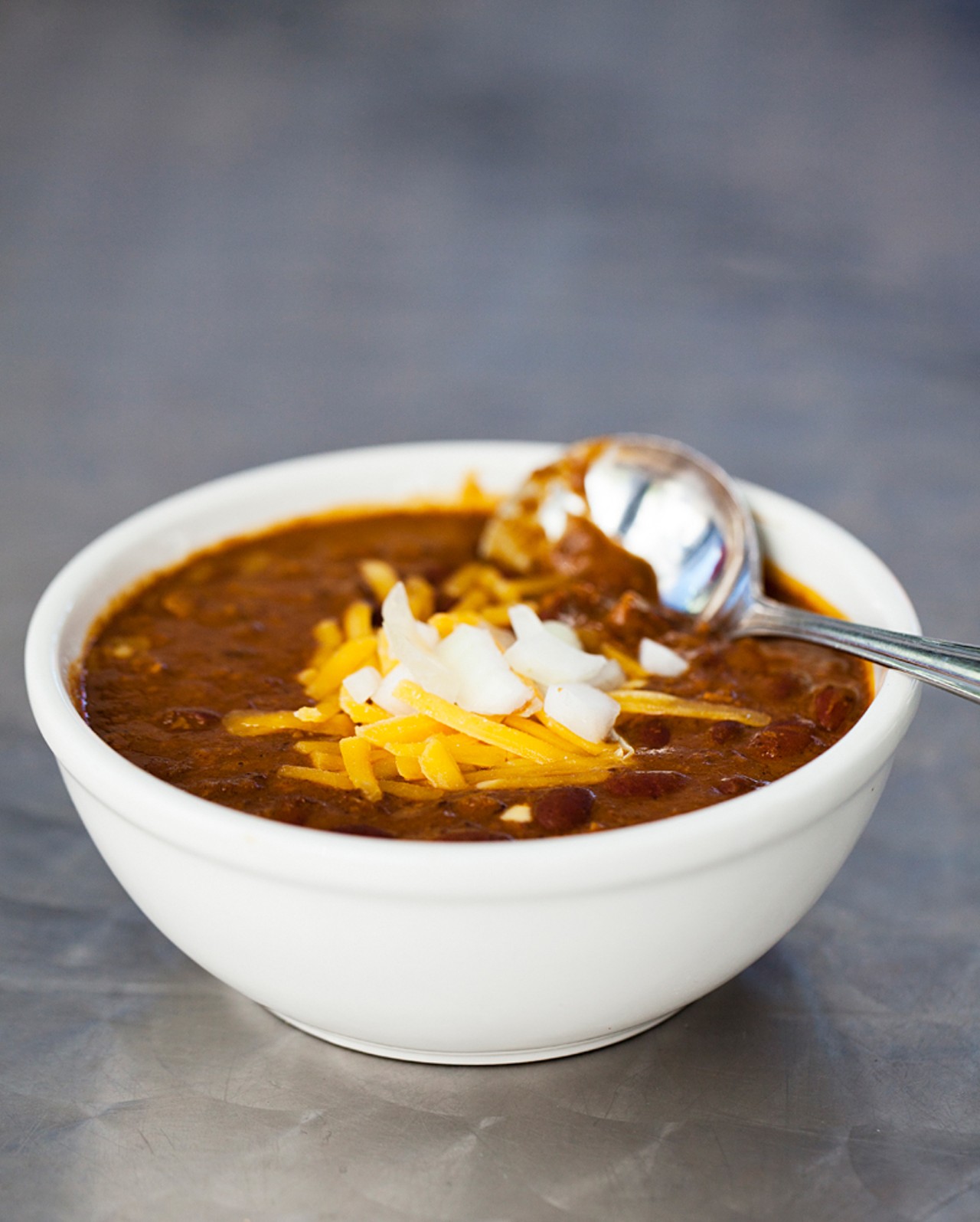 Bowl of chili with cheddar cheese and onions.