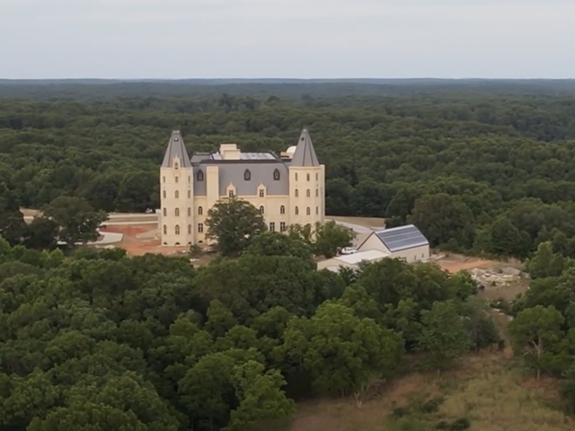 A gigantic, cream-colored, castle-looking structure sits in the middle of a wooded area.