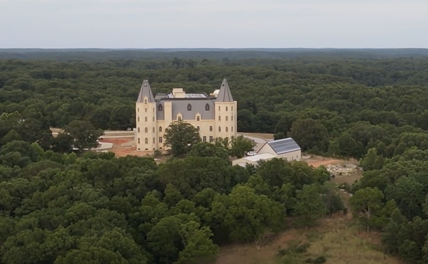 A gigantic, cream-colored, castle-looking structure sits in the middle of a wooded area.