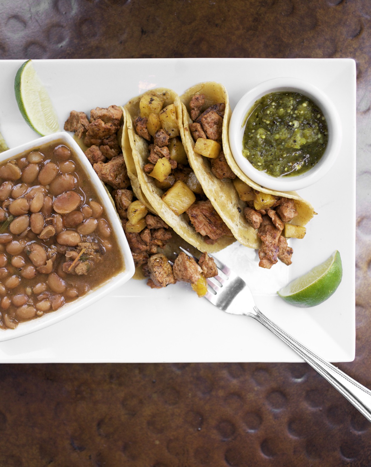 The TACOS al PASTOR are chile marinated pork tenderloin with grilled pineapple and cilantro in homemade corn tortillas, served with salsa verde and a side of Mexican beans and rice.