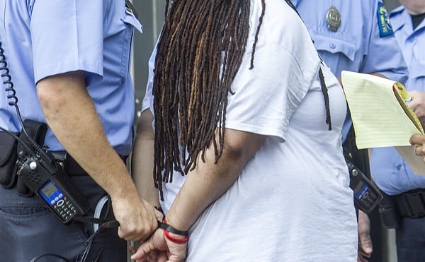 A police officer cuffs a Black woman.