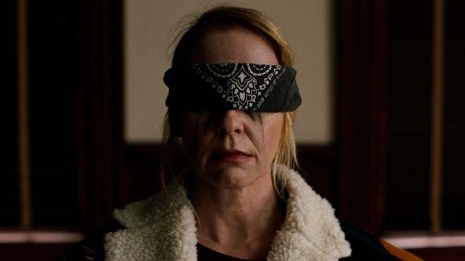 A film still depicting a woman from the shoulders up who is blindfolded.