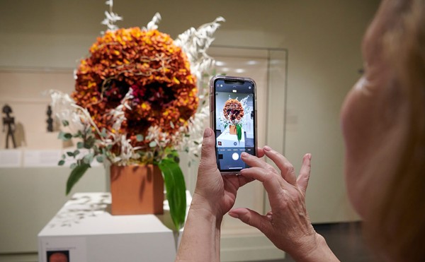 A person takes a photo of an orange flower display.