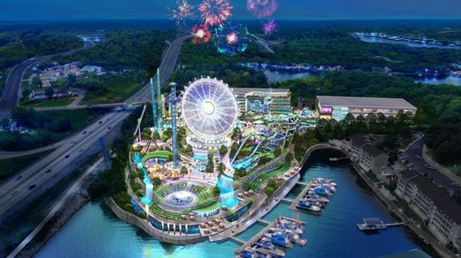 An aerial shot of the Lake of the Ozarks shows a brightly lit amusement park that features a Ferris wheel and plenty of rides on a lakefront property.