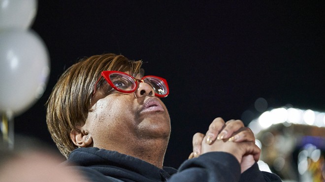 A woman with red glasses holds her hands together.