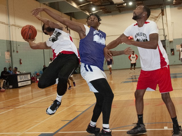 A player swerves away from the defenders as he goes up for a layup. Another player tries to block him.