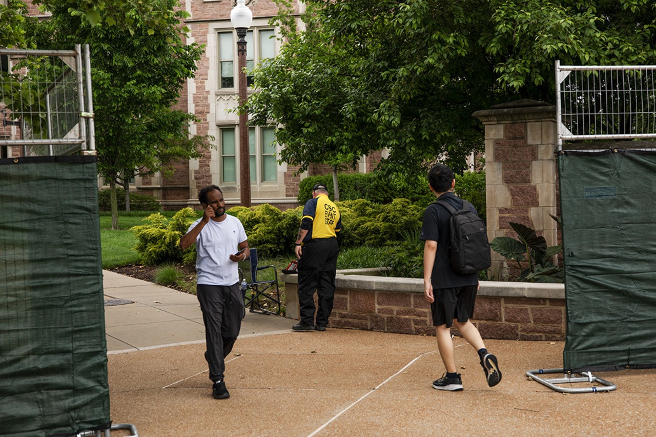 Students walk past an event staff worker monitoring the entrance to Wash U at the intersection of Skinker Boulevard and Forest Park Parkway.