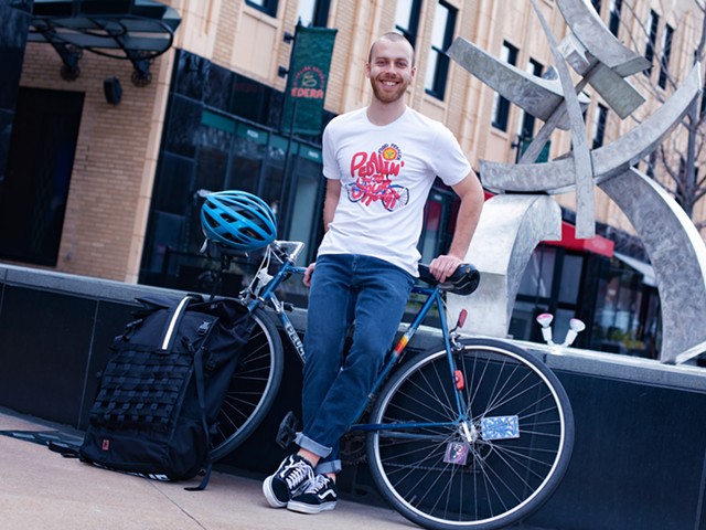 Alex Ward leans against a bike in front of a sculpture in the Central West End.