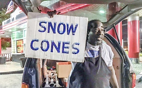 The St. Louis Candyman holds a sign that reads "SNOW CONES" in front of a van.