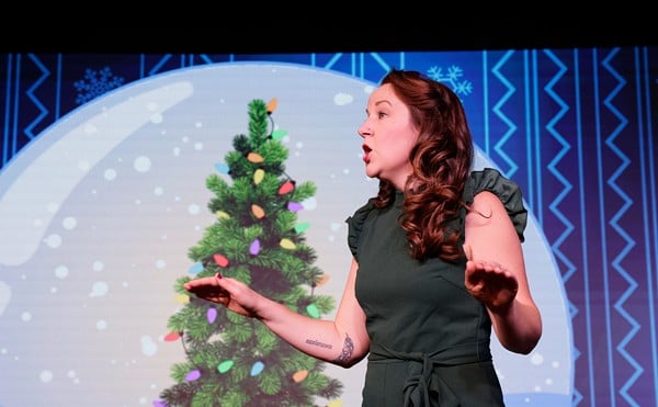 A woman stands on stage talking animatedly in front of a Christmas tree.