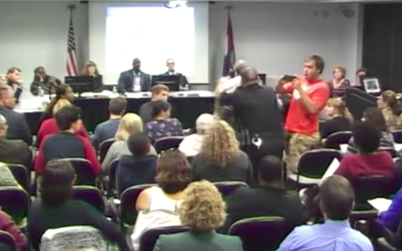 A man with a camera reacts as a St. Louis police officer knocks down Steve Taylor, an instructor attempting to speak at October 19's board of trustee meeting. - image via YouTube