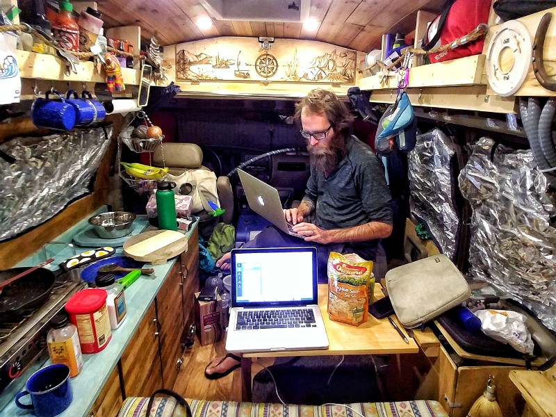 John Serbell works on his laptop after preparing a meal in the van's miniature kitchen. - Courtesy of John and Jayme Serbell