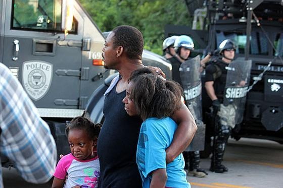 A family watches police in riot gear move into Ferguson in the early days of the August protests. - Danny Wicentowski