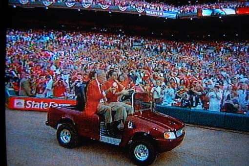 Stan Musial rides out in a customized Mercedes-Benz golf cart and shakes a baseball at the cheering fans.