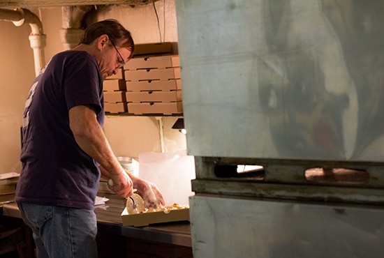 General manager Tom Nix slices up a steaming-hot pizza in the kitchen.