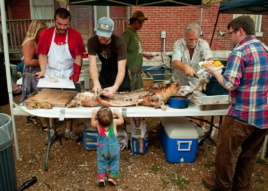 Brad "Mort" Munger (left) and John Joern (right) carve the first of two roasted pigs at the Off Broadway Pig Roast on Sunday. - Brian Heffernan
