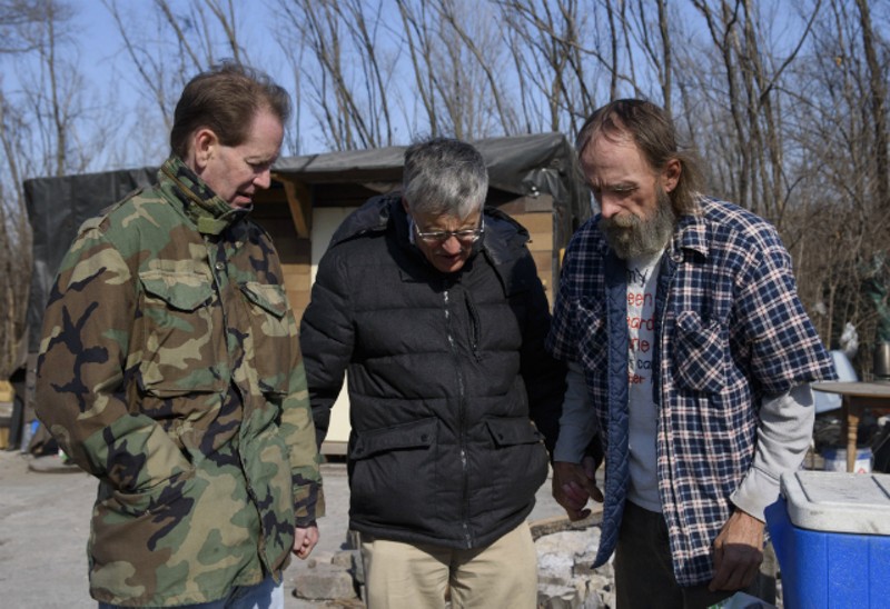 From left, Chris Ohnimus and Ray Redlich pray with Robert Gibson at homeless encampment in 2018 in East St. Louis. - NICK SCHNELLE