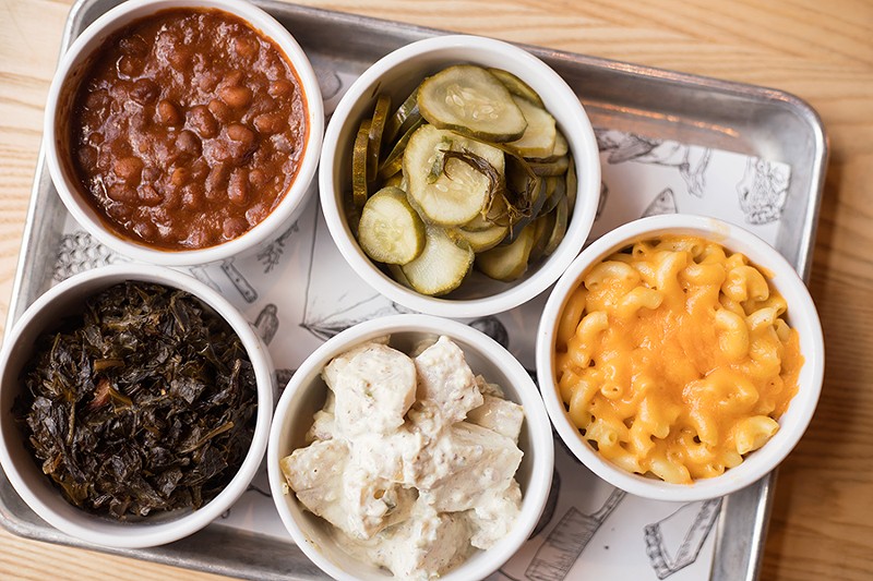 A selection of sides: pit beans, fresh dill pickles, mac ‘n’ cheese, candied bacon-jalapeno potato salad, ham hocks with collard greens. - MABEL SUEN