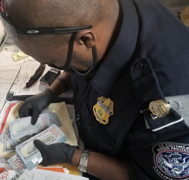 A customs agent counts a stack of fake $100 dollar bills. - U.S. Customs and Border Protection