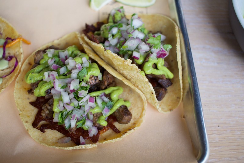 Carne Asada tacos feature crunchy Chihuahua cheese, avocado, and black sauce.  - Cheryl Baher
