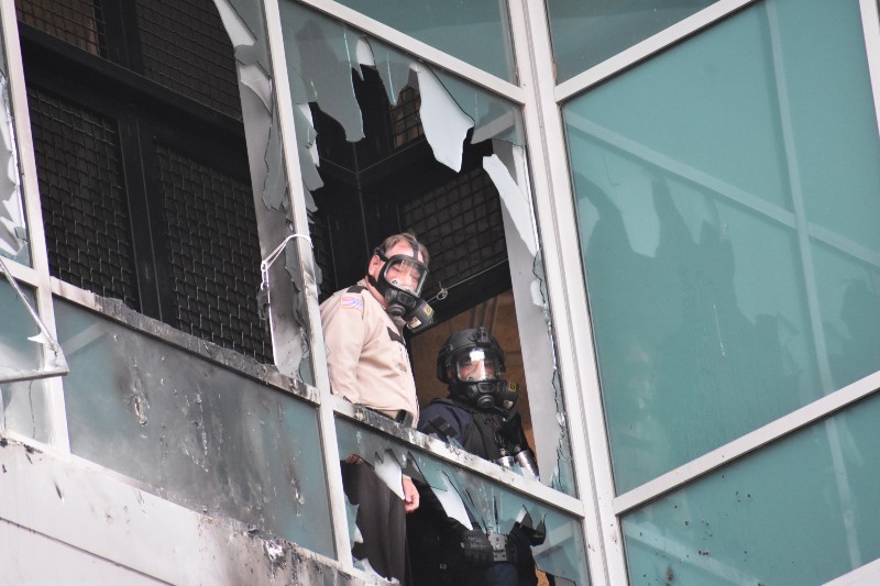A St. Louis Sheriff's deputy and police SWAT supervisor look out of shattered window on February 6, 2021, at the City Justice Center.