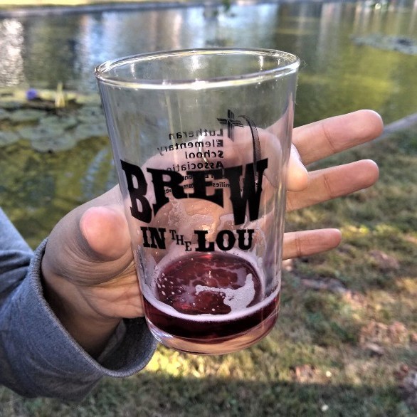 A hand holds a Brew in the Lou beer glass.