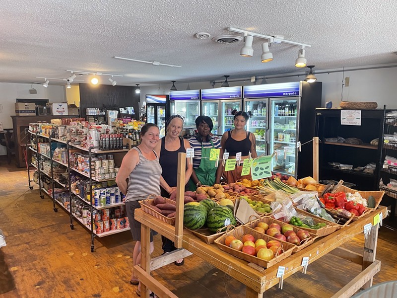 Ranata Frank, Beth Neff, Chrissy Kirchhoefer and Grace Smith stand in front of a fresh produce section with refrigerators and aisles of food behind them.