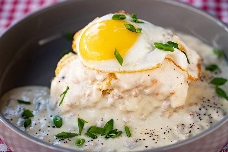 A biscuit topped with an egg and surrounded by gravy.