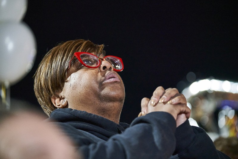 A woman with red glasses holds her hands together.